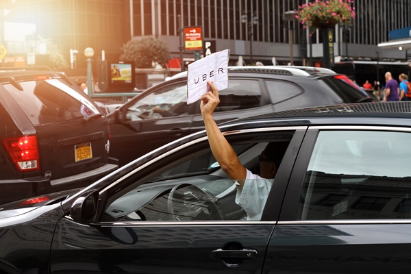 Uber driver holding a sign out of a car window in busy New York City traffic.