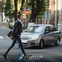 A New Rochelle pedestrian crosses the street in a crosswalk in front of a grey car