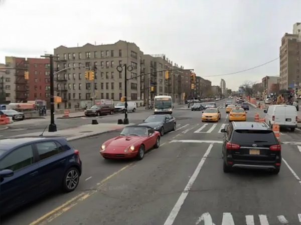 A busy street in the Bronx with a mix of traffic, including a red convertible and a city bus, framed by large, multi-story apartment buildings under an overcast sky.